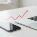 Smartphone and laptop with an upward trending arrow symbolizing the tariffs impact on technology and rising costs.
