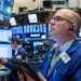 A stock trader shows concern while watching market data decline on electronic screens, illustrating the financial impact of tariffs.