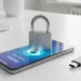 A silver metal padlock sits on a smartphone screen next to an external USB drive on a white desk surface.