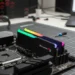 G.Skill Ripjaws M5 RGB memory sticks sit in a black motherboard on a grey grid mat next to a screwdriver and a laptop.