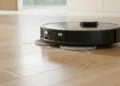 A black Dreame L50 Ultra robot vacuum and mop actively cleaning fine dust and debris off a light hardwood floor using its dual spinning mop pads.