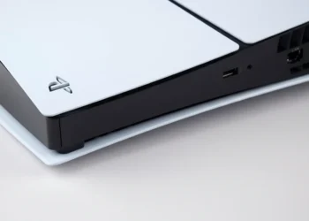 A close-up photograph captures the white outer panel and black center strip of a PlayStation 5 console on a neutral background.