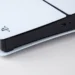 A close-up photograph captures the white outer panel and black center strip of a PlayStation 5 console on a neutral background.