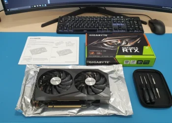 A Gigabyte GeForce RTX 3060 graphics card unboxed on a blue desk mat with its retail box, manual, and a small precision screwdriver kit.
